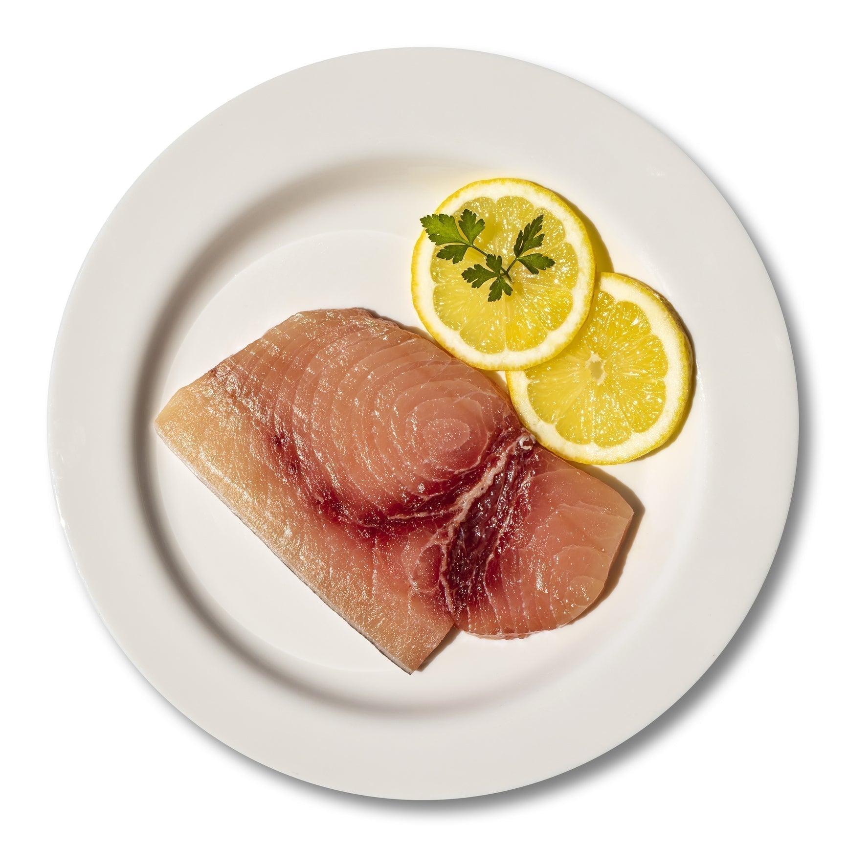 Thick dry-aged swordfish steak on a grill with char marks, ready to serve with lemon and herbs