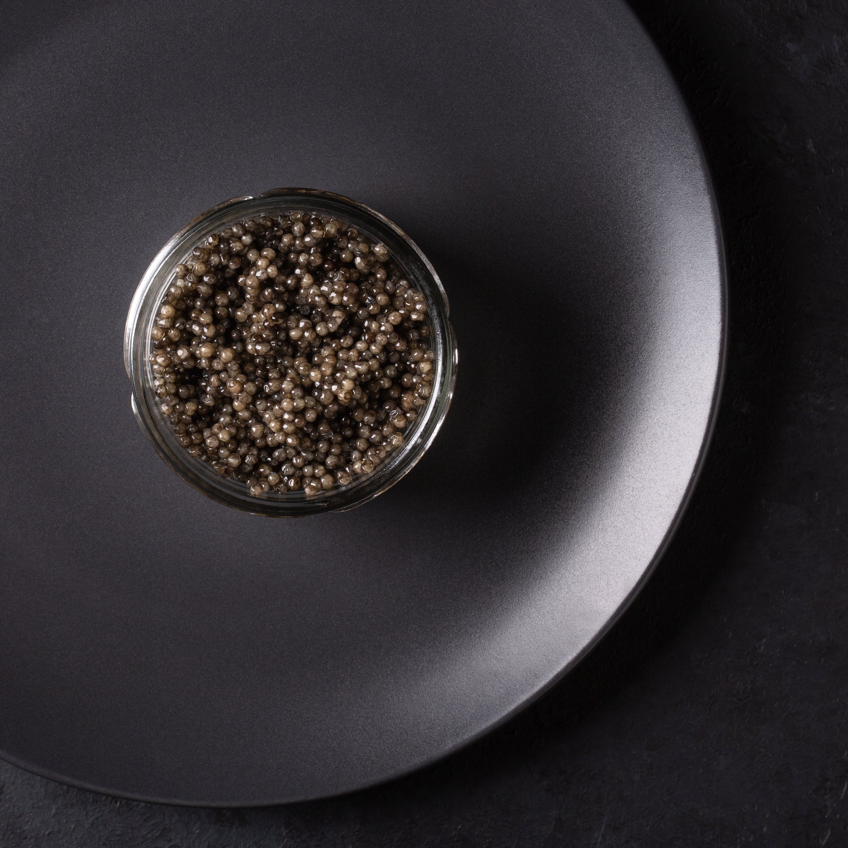 Premium beluga caviar pearls in an open tin with a mother-of-pearl spoon on a dark marble surface