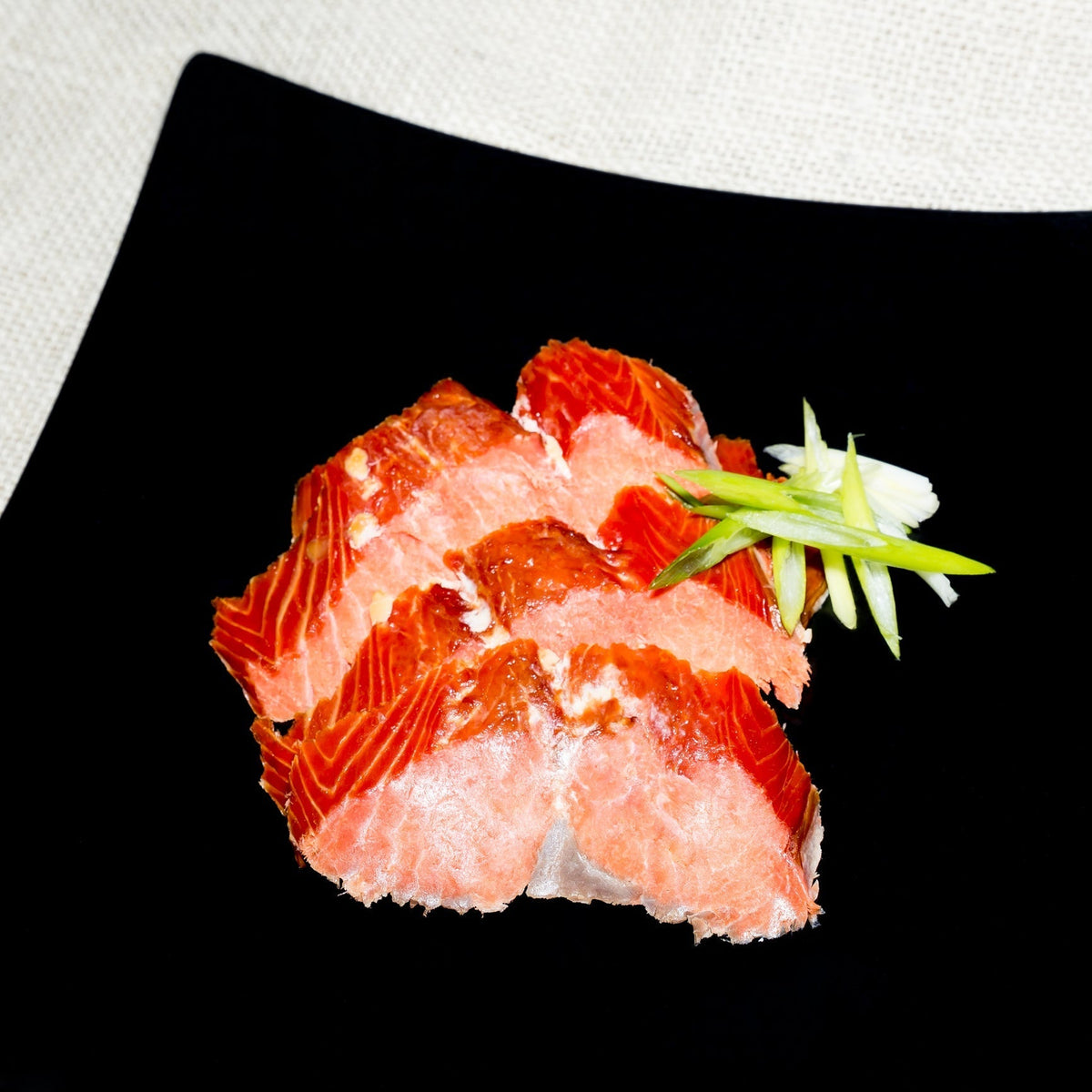 Thinly sliced cold-smoked wild Alaskan salmon on a wooden board with capers, red onion, cream cheese, and lemon