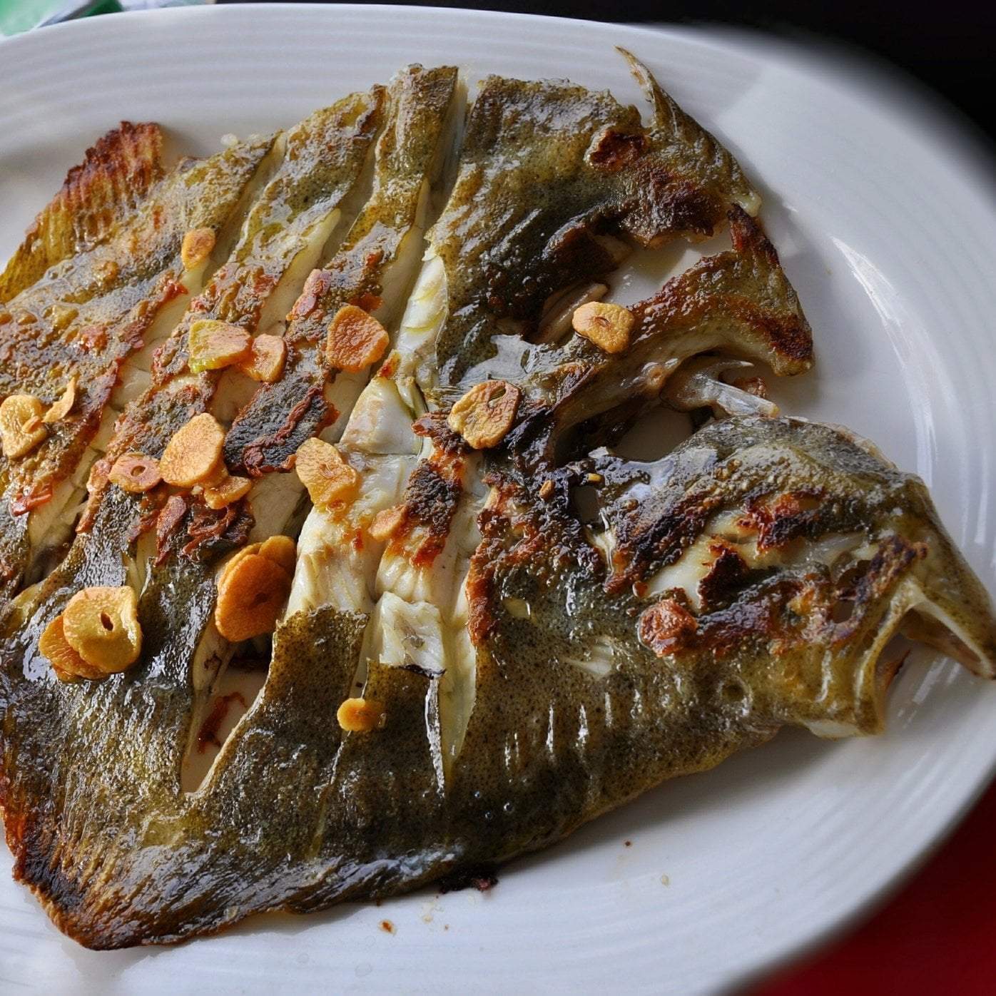 Fresh flounder fillet on a white plate with lemon wedges and fresh herbs, showing the fish's white, flaky flesh — a lean, mild-flavored flatfish