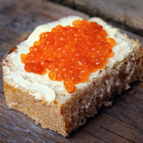 Vibrant red salmon roe served in a glass bowl on crushed ice with blinis and crème fraîche