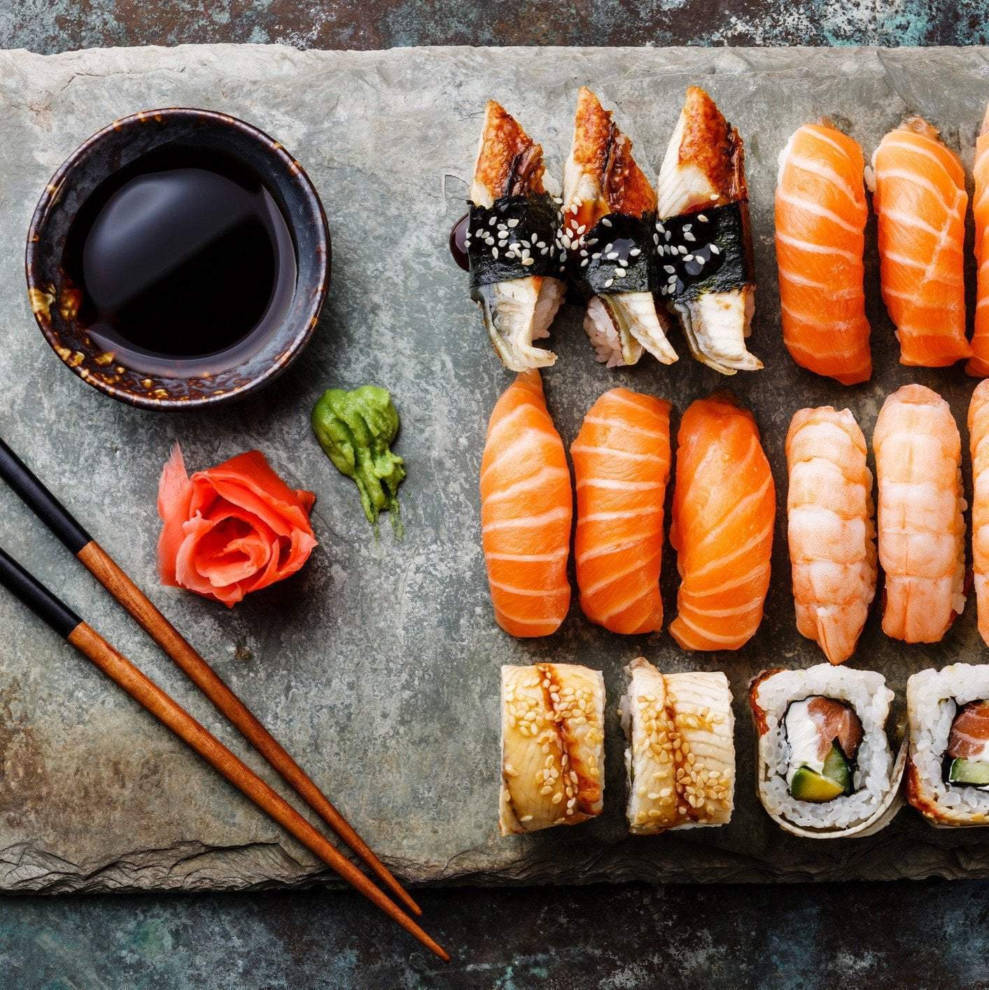 Assorted sushi rolls and sashimi with salmon, tuna, and avocado on a wooden board