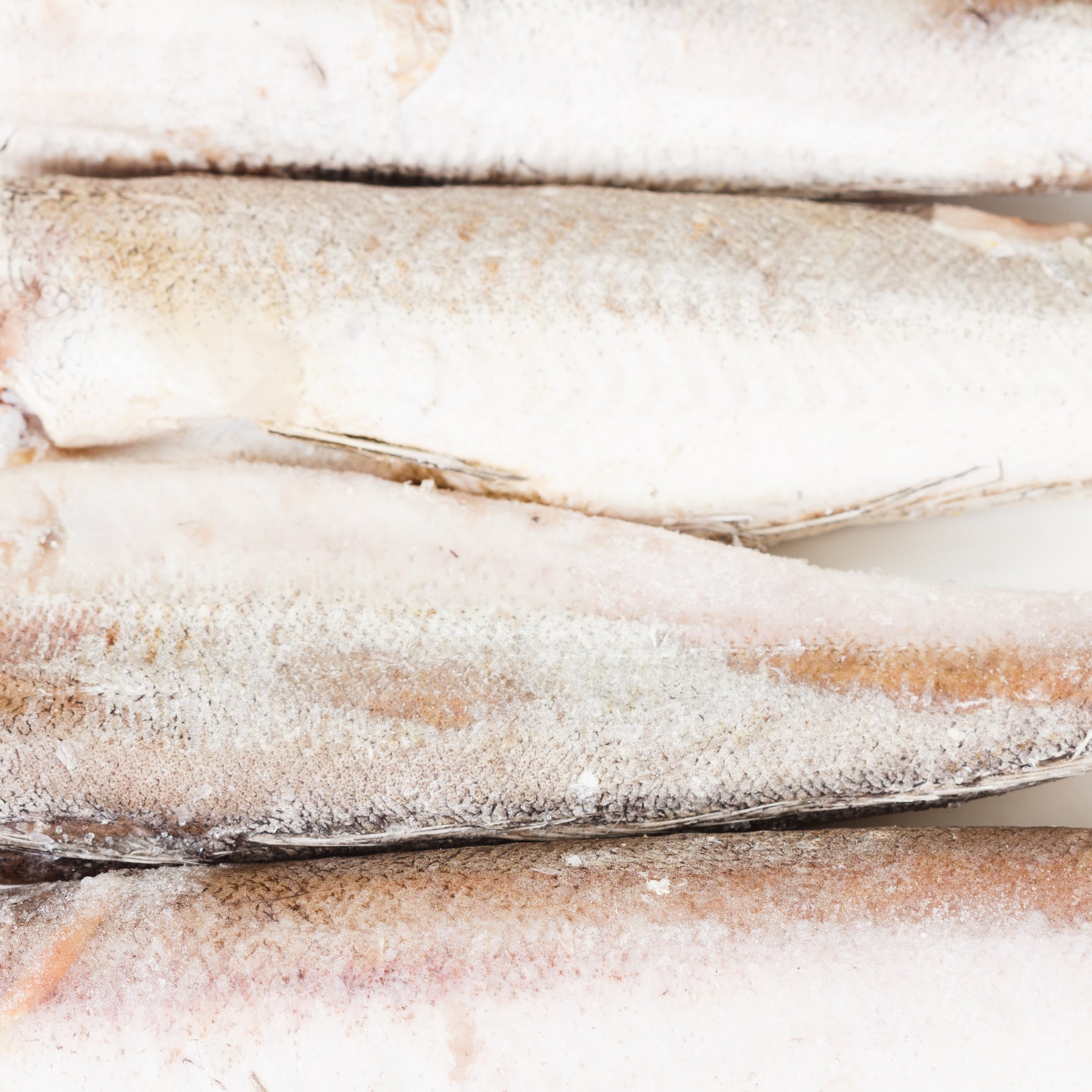 Fresh Pacific Whiting fillets on a wooden cutting board with lemon, garlic, and fresh herbs for a family dinner