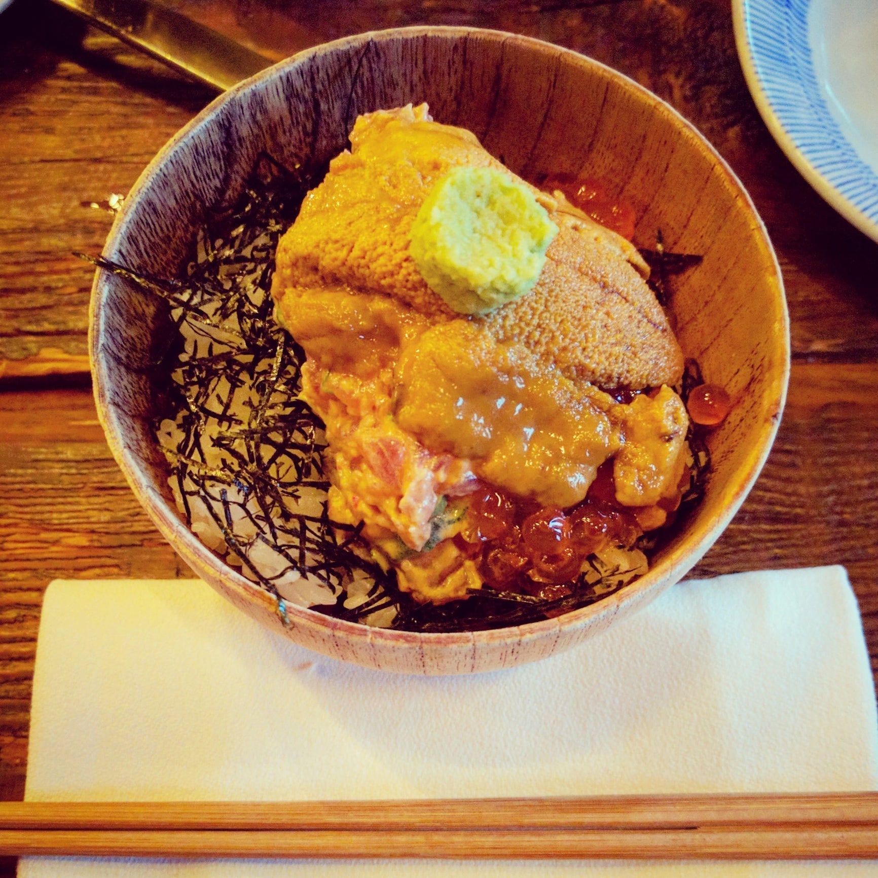 Chef placing fresh sea urchin uni on sushi rice nigiri on a dark slate plate