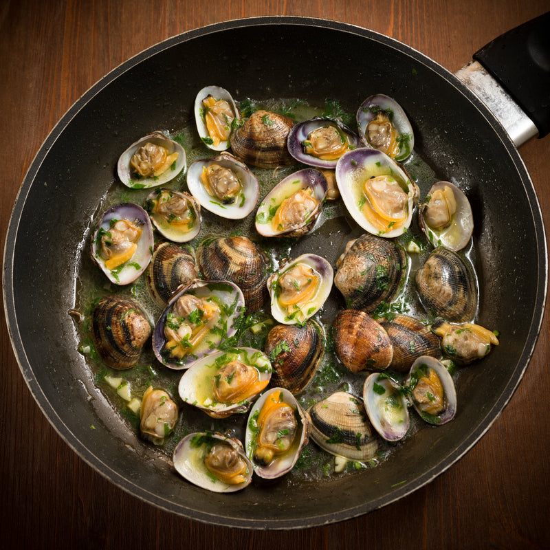 Clams being scrubbed under cold running water and soaked in salted water to remove sand and grit before cooking