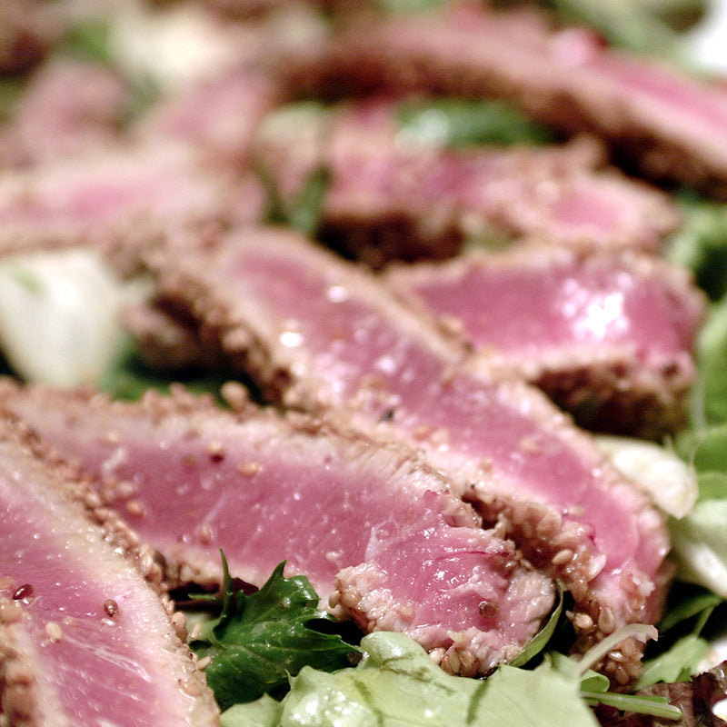 Sliced smoked tuna on a wooden board with herbs and lemon