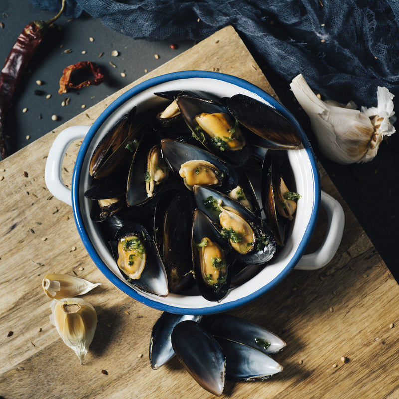 Freshly smoked mussels on a wooden board with herbs, garlic, and lemon