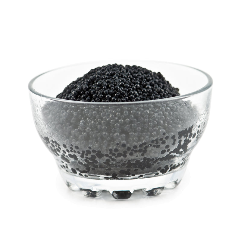 Golden-gray paddlefish caviar served on a mother-of-pearl spoon with blini and crème fraîche on a dark slate board