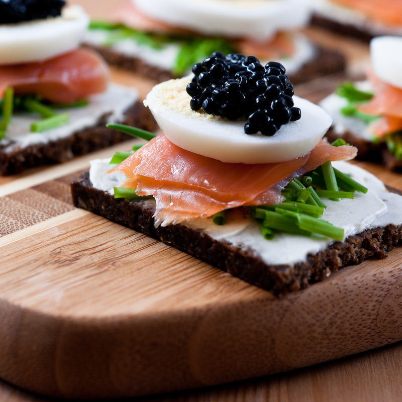 Siberian sturgeon caviar pearls in a glass dish on crushed ice served with blinis and crème fraîche