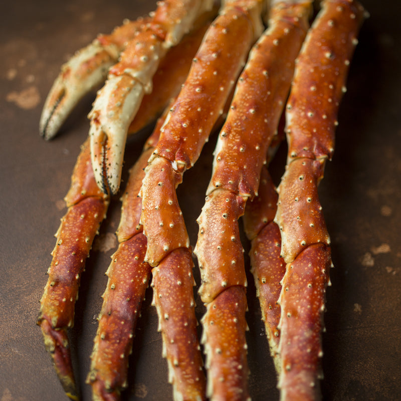 Steamed king crab legs with garlic butter sauce and lemon wedges on a rustic wooden serving board
