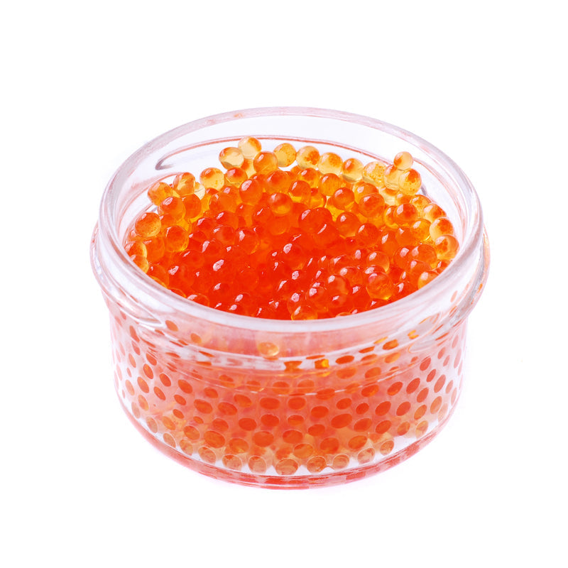 A close-up of vibrant orange salmon roe pearls glistening in a small glass bowl, surrounded by fresh herbs and lemon slices