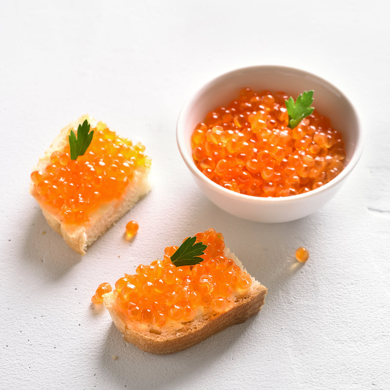 Two varieties of Chinook red caviar side by side in glass bowls with blinis and champagne