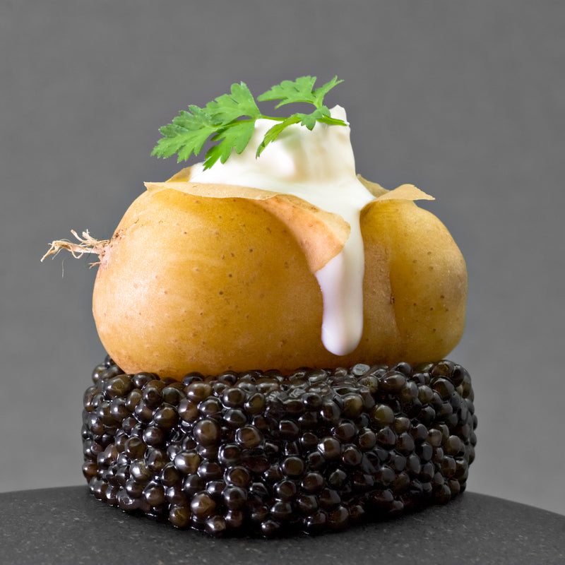 Elegant blinis topped with white sturgeon caviar and crème fraîche on a dark slate board