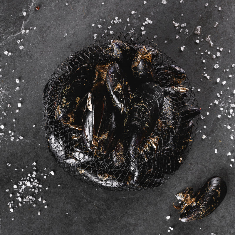 Fresh mussels in a black pot with steam rising, garnished with herbs on a rustic table