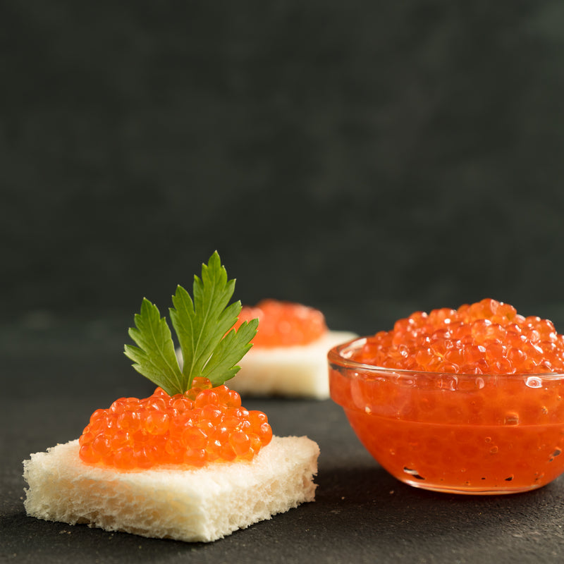 Caviar martini in a chilled glass garnished with golden trout roe on a mother-of-pearl spoon, with champagne flutes and caviar tins in the background