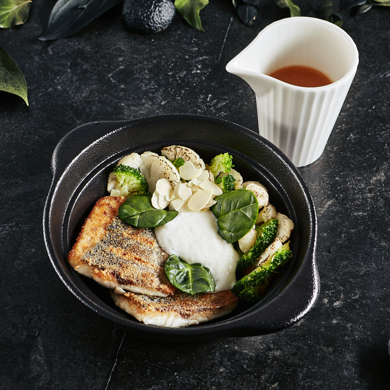 Pan-seared branzino fillet with lemon slices and fresh herbs on a white plate