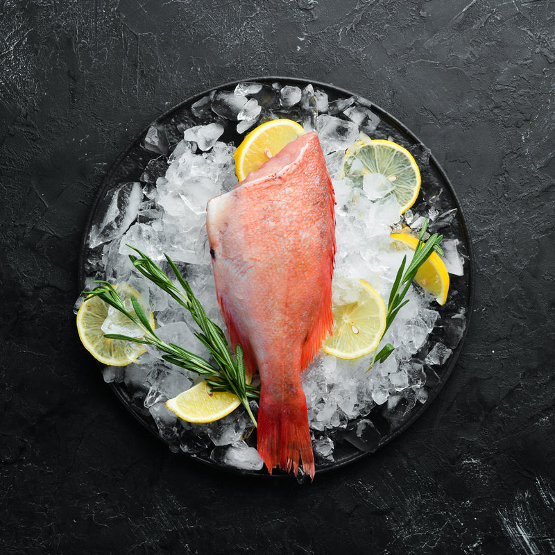 Whole grilled red snapper with herbs and lemon on a serving platter