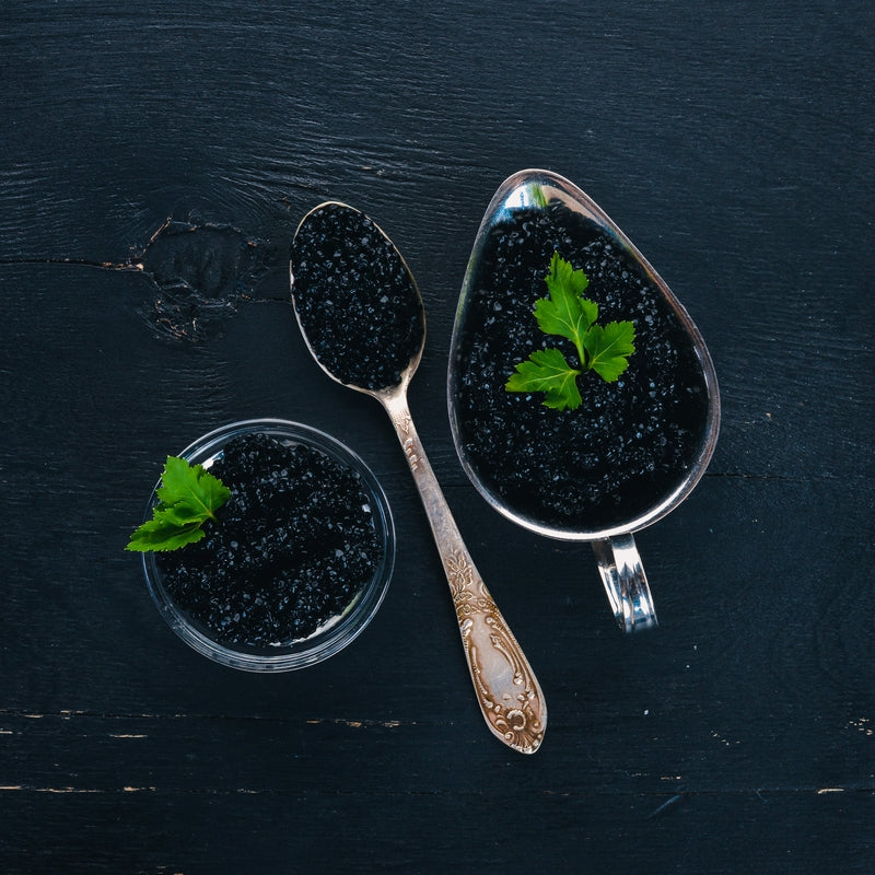 Side-by-side comparison of paddlefish caviar and traditional sturgeon caviar on a dark slate board with serving spoons