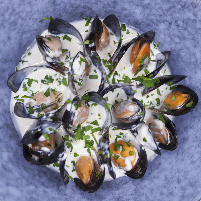 Fresh blue mussels in a white bowl with parsley garnish on a rustic wooden surface