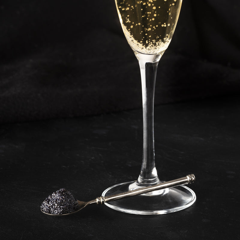 An elegant champagne flute with salmon roe floating on top of a sparkling cocktail, garnished with an orange twist on a dark background