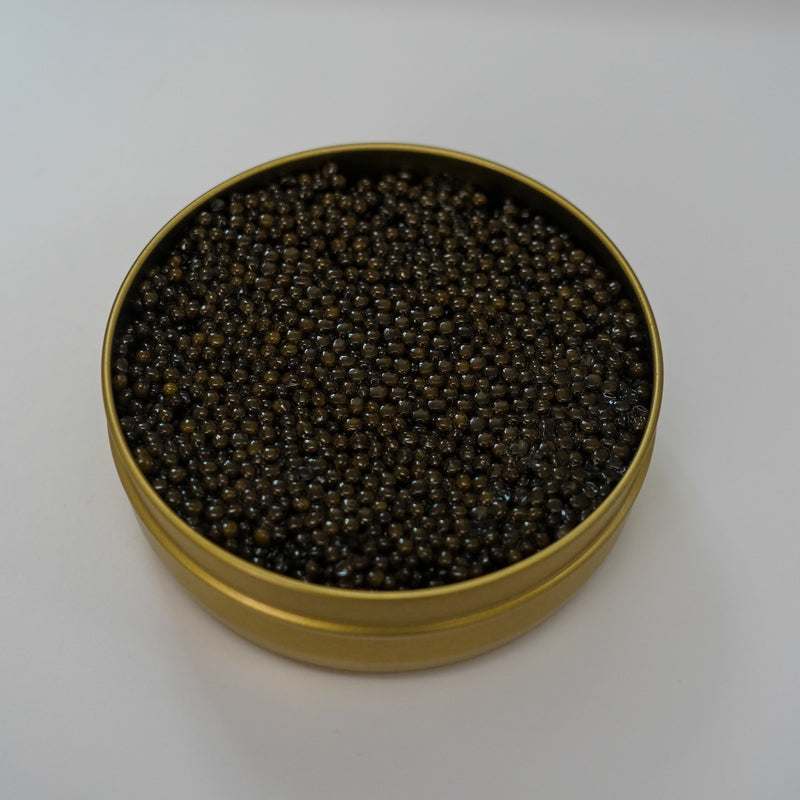 Elegant serving of paddlefish caviar on mother-of-pearl spoon with blini and crème fraîche on a dark slate board