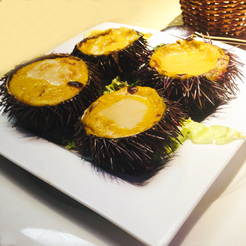 Fresh sea urchin opened to reveal bright orange uni roe inside the spiny shell on a dark surface