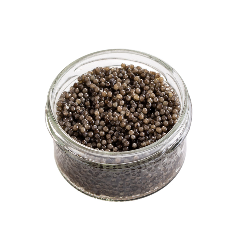 Close-up of glistening gray-black paddlefish caviar pearls served on a mother-of-pearl spoon with blini and crème fraîche