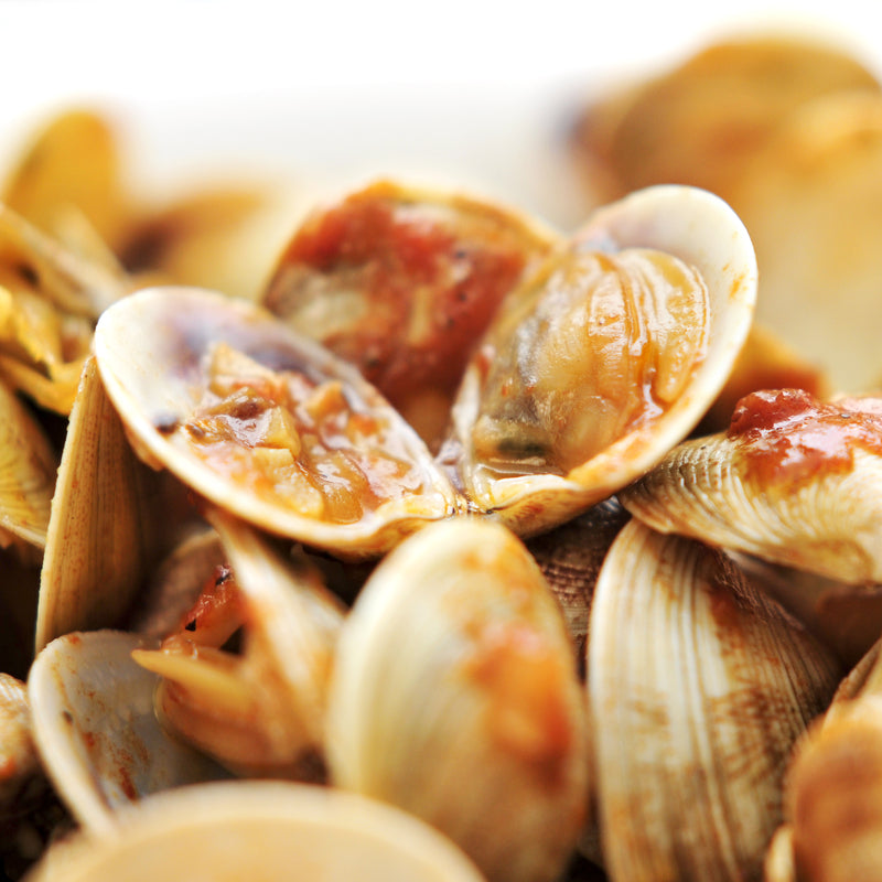 Fresh Manila clams in the shell arranged on crushed ice at a seafood market, showing their distinctive patterned shells and tightly closed valves