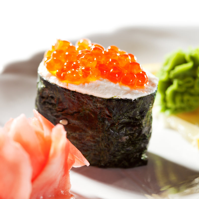 Assorted ikura dishes including blini with salmon roe, ikura pasta, and canapés arranged on a dark serving board