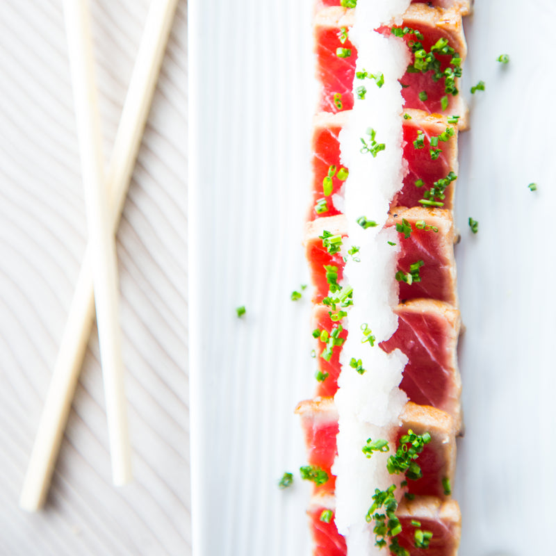 Pre-smoked tuna fillet being flaked into a Mediterranean pasta dish with capers and lemon