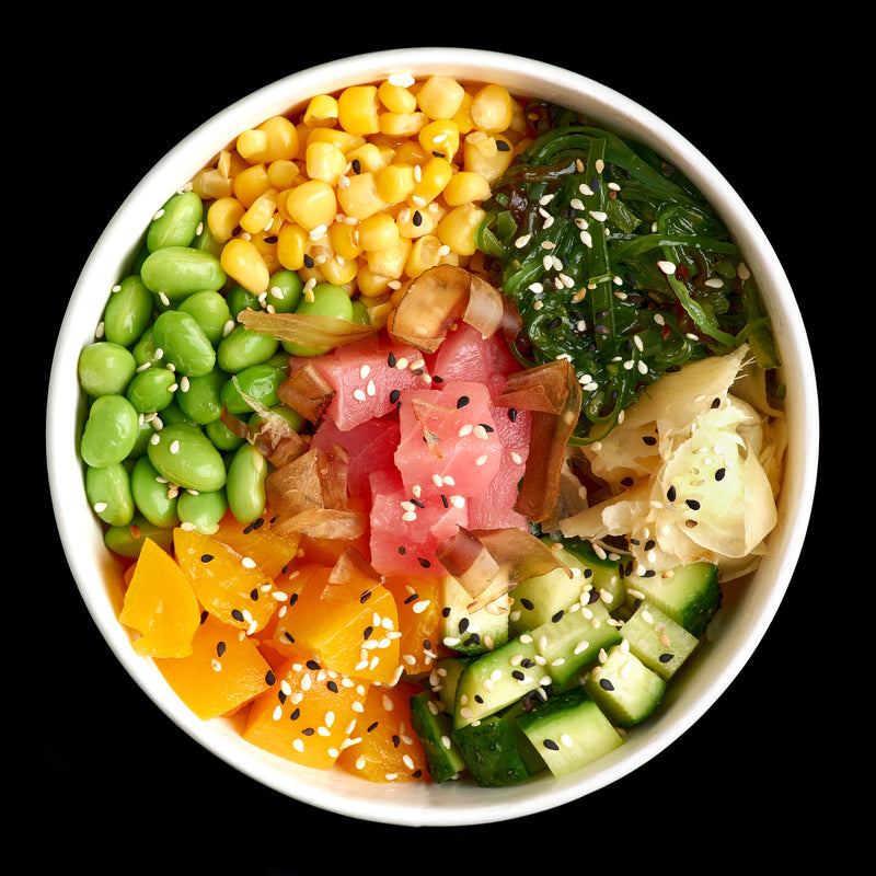 Fresh sushi-grade tuna being sliced into cubes for a Hawaiian poke bowl, surrounded by ocean-inspired ingredients