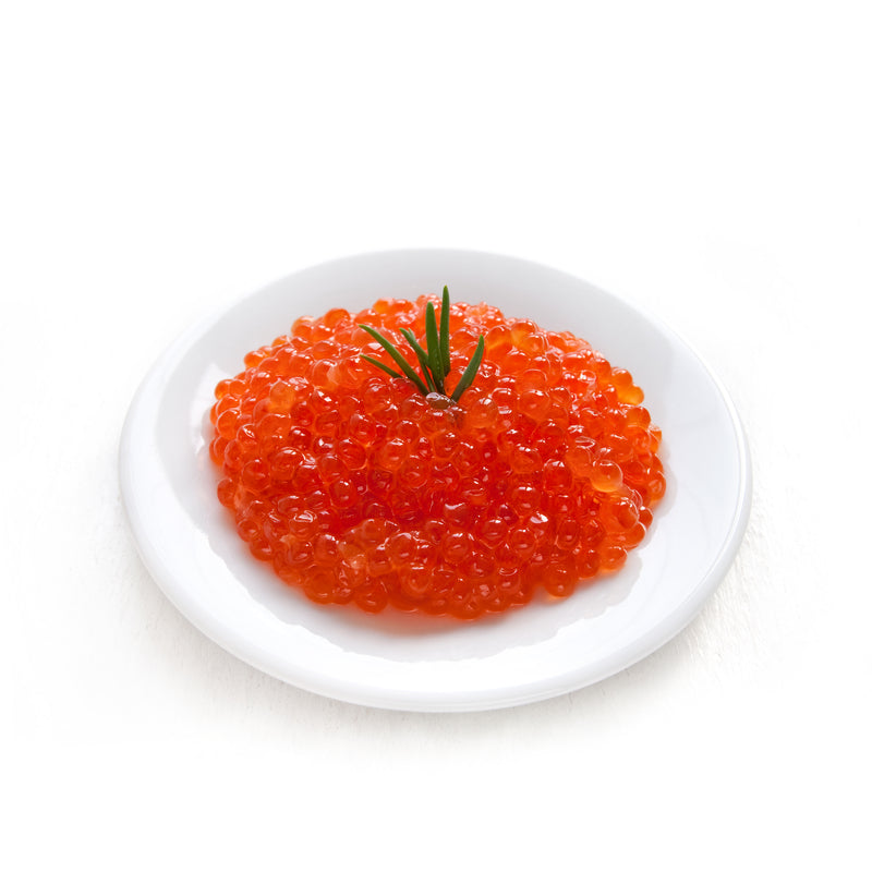 Vibrant orange ikura salmon roe pearls in a ceramic bowl beside sushi rice and nori on a wooden board