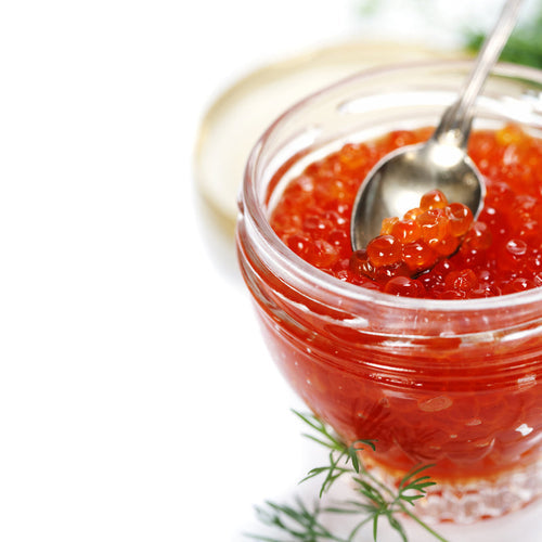 Glass jar of bright red salmon roe with a silver spoon scooping caviar, garnished with fresh dill on a white background