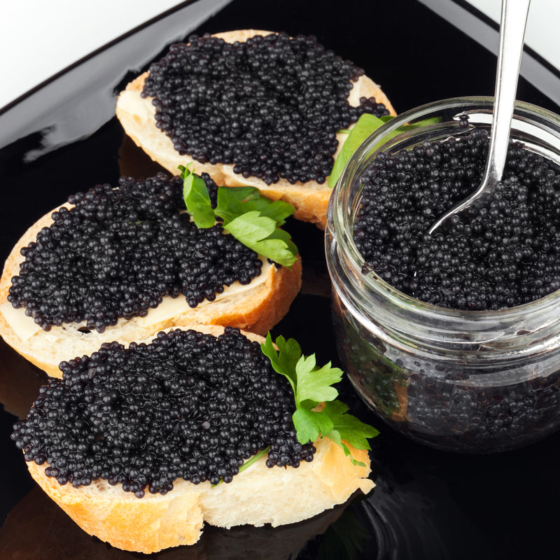 Osetra caviar tin stored on crushed ice with a mother-of-pearl spoon and elegant serving dish