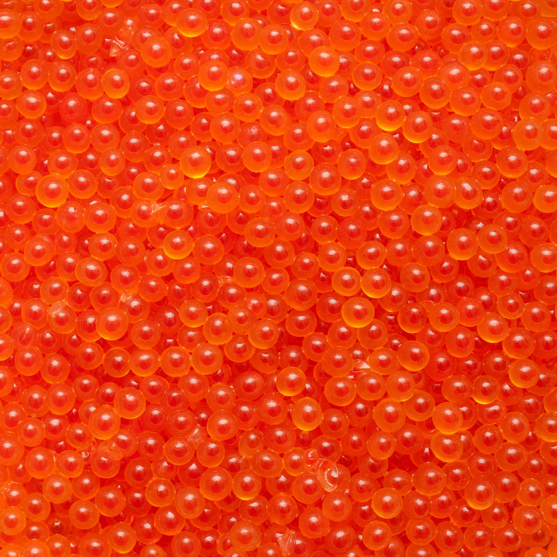 Close-up of vibrant orange-red salmon roe in a glass jar with a mother-of-pearl spoon on a dark surface