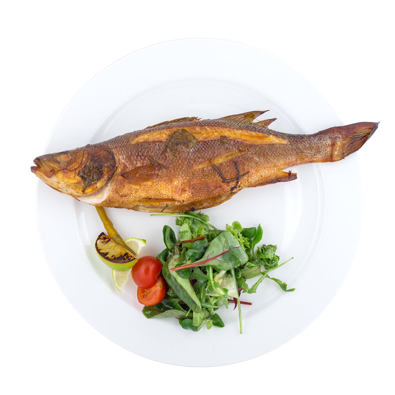 Whole grilled Branzino on a platter with lemon slices and fresh herbs