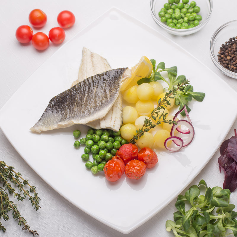 Golden pan-seared branzino fillet with crispy skin, garnished with lemon and fresh herbs