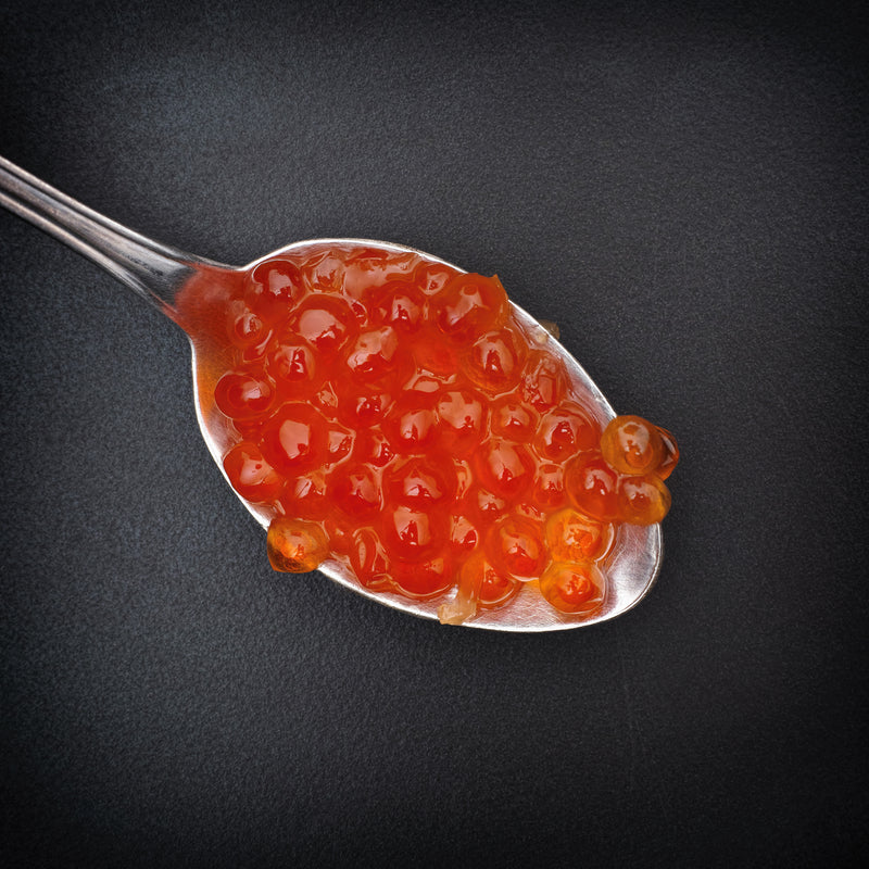 Large glistening King Salmon red caviar pearls in a glass bowl with a mother-of-pearl spoon