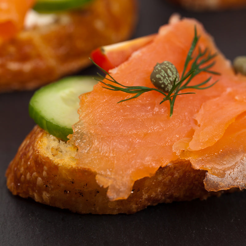 Thinly sliced lox and cold-smoked salmon on a wooden board with cream cheese, capers, red onion, and lemon wedges