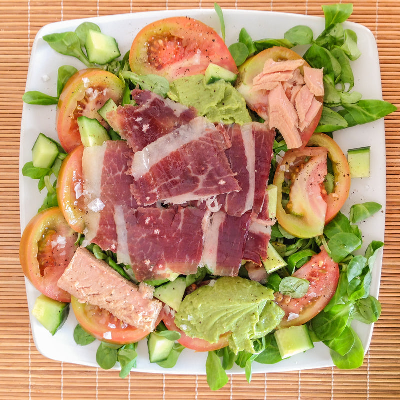Thinly sliced smoked ahi tuna arranged on a white plate with capers, fresh herbs, lemon wedges, and a drizzle of olive oil