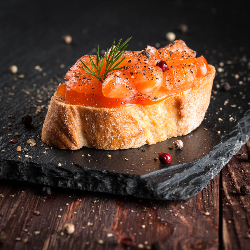 Thinly sliced cold-smoked salmon on a wooden board with capers and lemon