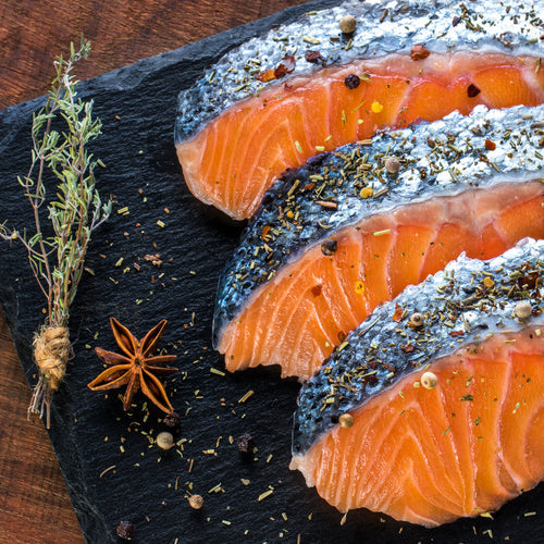 Grilled sockeye salmon fillet with lemon slices and fresh herbs on a wooden board