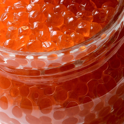 Close-up of a glass jar filled with bright orange-red salmon roe