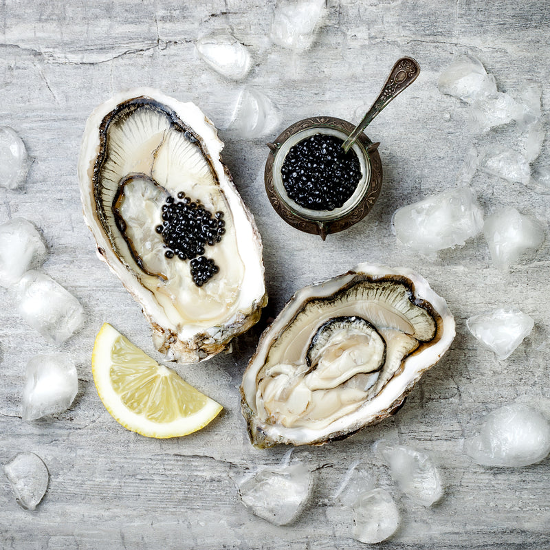 Beluga caviar served in a glass dish on ice alongside chilled vodka shots and blinis