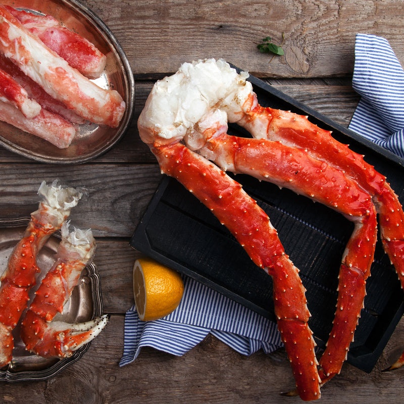Steamed Alaskan king crab legs served with dipping sauces on a wooden board