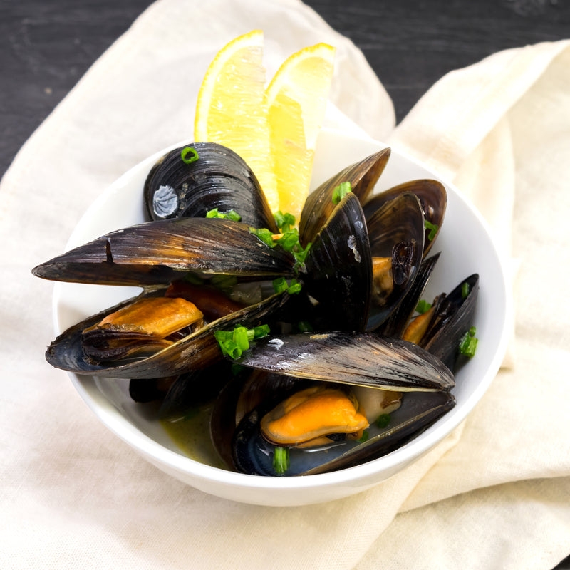 Fresh blue mussels steamed open in a white wine broth with garlic, shallots, and parsley in a large pot