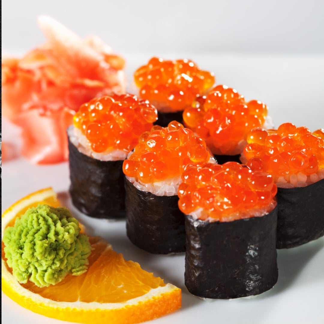 Assortment of fish roe varieties including salmon ikura, tobiko, and trout caviar displayed on ice with blinis and crème fraîche