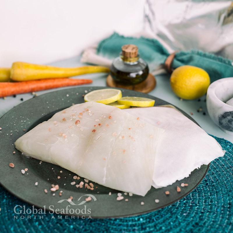 Raw halibut fillet portions on a gray plate with lemon slices and seasoning