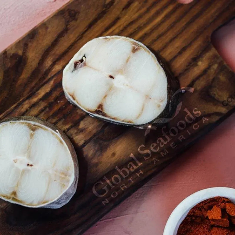 Two raw black cod steaks on a wooden board.