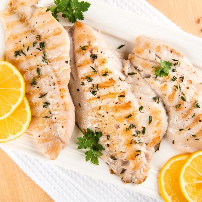 Grilled rockfish fillets with garlic, fresh herbs, and lemon wedges on a grill with char marks